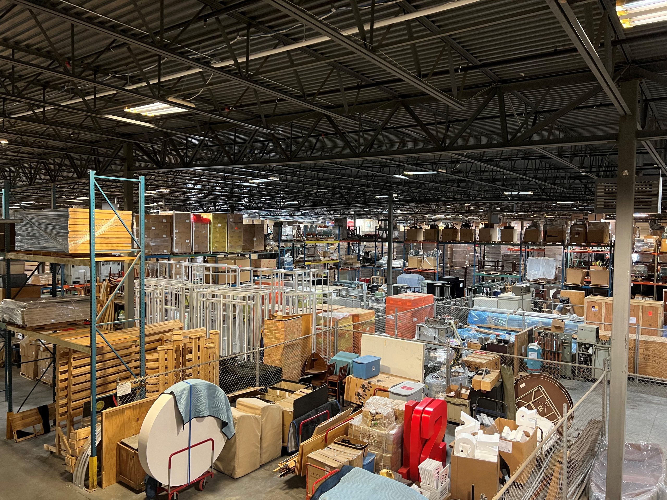 A shot of the warehouse interior showing packed shelves with various furniture items, boxes, metal racks, tables, and other items.